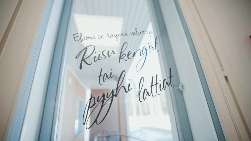 Tekstiteippaus lasiovessa, jossa lukee "Elämä on täynnä valintoja. Riisu kengät tai pyyhi lattiat."